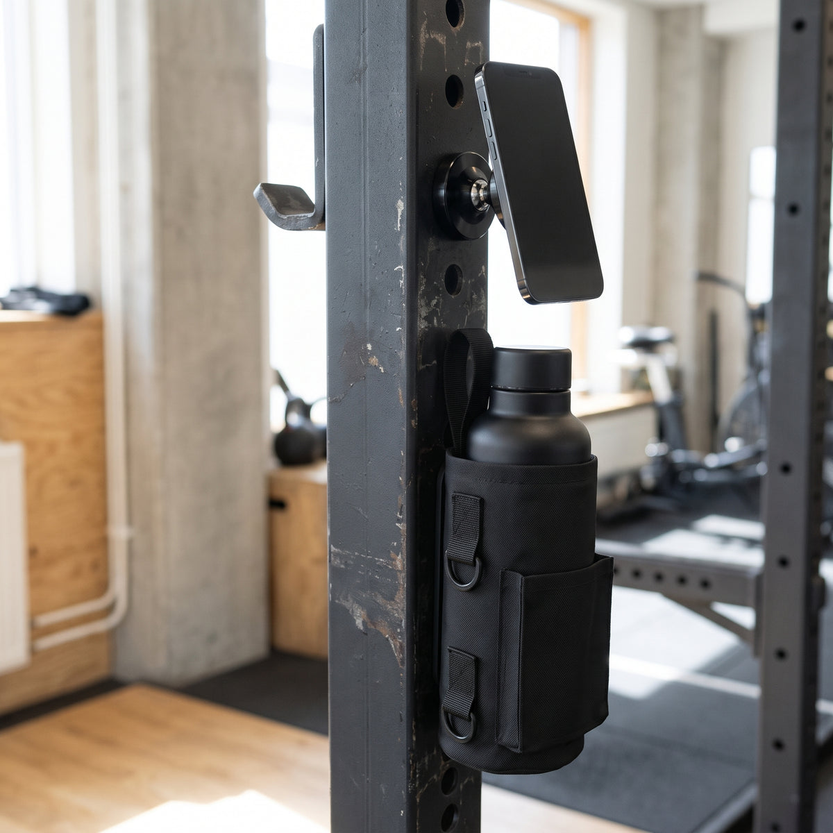 Gympaketet i bruk: mobilen sitter på den svarta magnetiska mobilhållaren och vattenflaskan i gymväskan på stålramen
