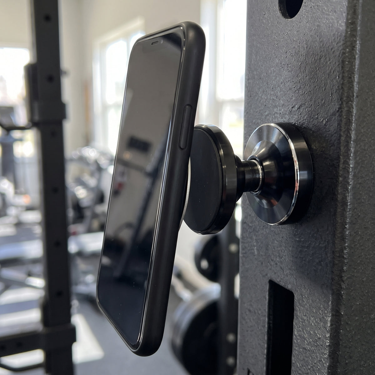 Gympaketet – närbild på den svarta magnetiska mobilhållaren med mobilen på, fäst mot maskinens stålram