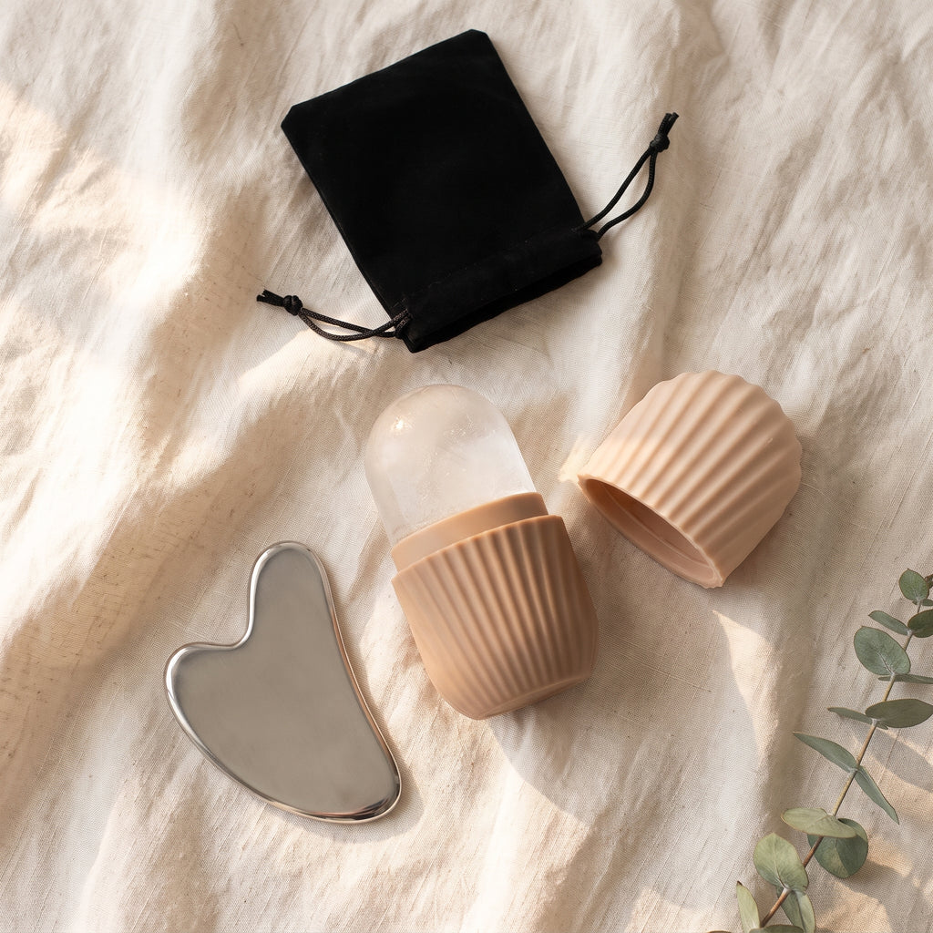 Beige – ice roller med isform i beige silikon, lock och hjärtformad gua sha i stål på ljust linne i morgonljus