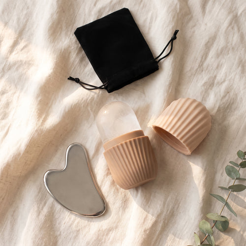 Beige – ice roller med isform i beige silikon, lock och hjärtformad gua sha i stål på ljust linne i morgonljus