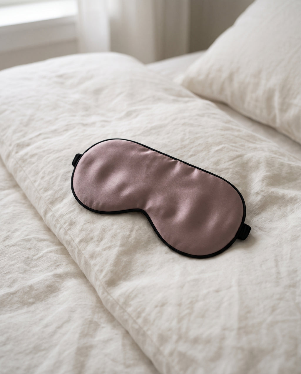 Ljusblockerande sovmask i mullbärssilke i dammig mauve på neutral bakgrund i ett enkelt sovrum