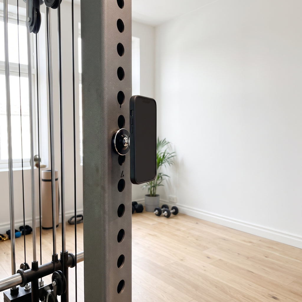 Den svarta magnetiska mobilhållaren på gymställningens stålram med mobilen fäst, i ett ljust svenskt gym