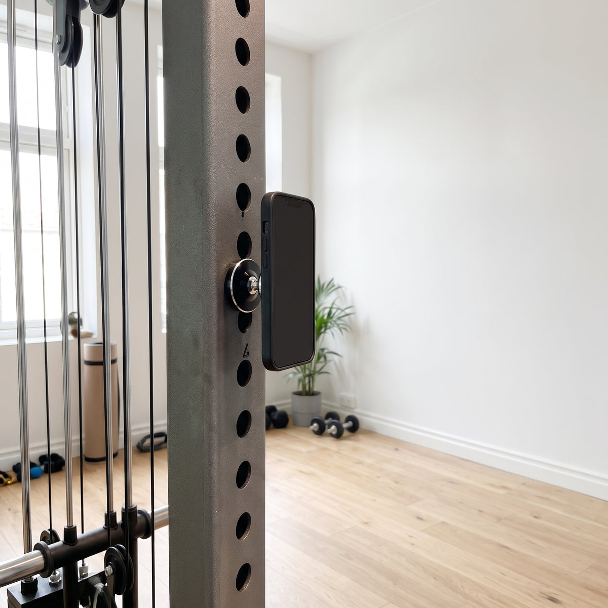 Den svarta magnetiska mobilhållaren på gymställningens stålram med mobilen fäst, i ett ljust svenskt gym