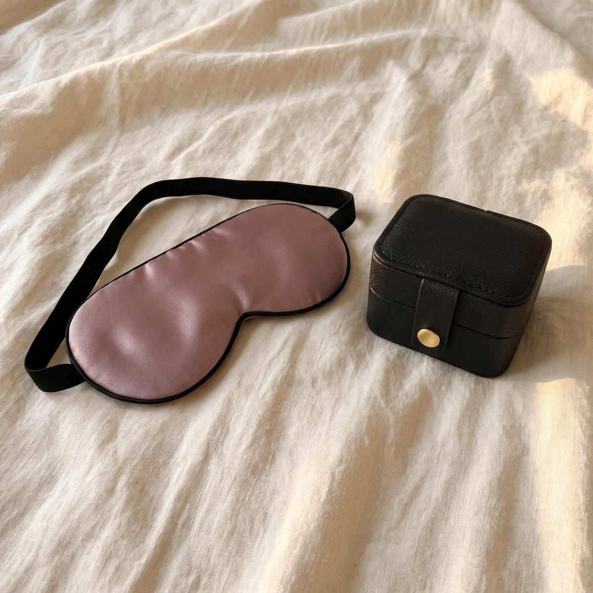 Resesetet: sovmask i mauve mullbärssilke och svart ringask för resan tillsammans på en linnesäng