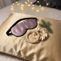 Silkesgåvan: sovmask i mauve mullbärssilke och två silkesscrunchies i champagne, fotograferade på ett silkesörngott i guld (örngottet ingår inte)