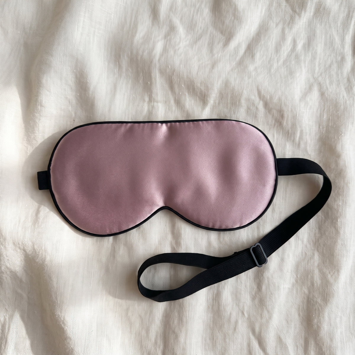 Sovmask i mullbärssilke i mauve, ingår: en sovmask med elastiskt band, liggande på ljus bakgrund